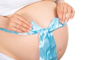 Close-up, blue bow on the naked belly of a pregnant woman Close-up, blue bow on the naked belly of a pregnant woman